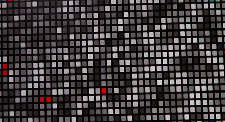 A grid of gray squares, varying in shade from light to dark gray, are arranged on a black background creating an abstract, data-like pattern with a few scattered red squares that add a focal point.