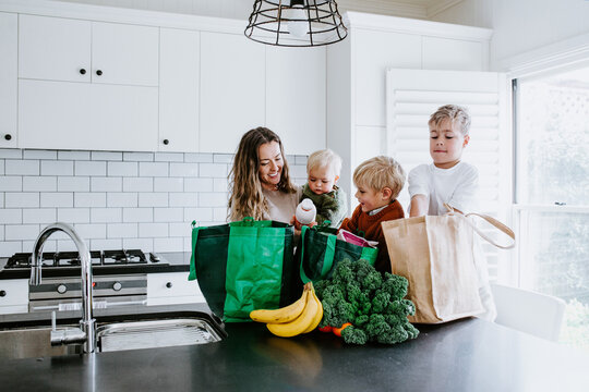 Mother with young boys unpacking groceries on the countertop in the kitchen