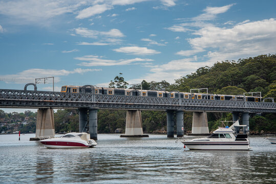 Train going over the rail bridge at Como in Sydney with moored boats in the foreground.