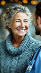 A happy senior woman with gray hair and blue eyes smiles warmly while talking to a person in a blue medical uniform.