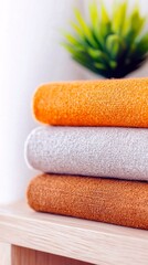 A close-up, vertical shot of three folded towels stacked on a wooden shelf, with a blurred green plant in the background.