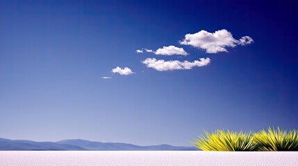 A bright, clear day with a vast blue sky dotted with fluffy clouds, featuring a patch of vibrant green grass in the foreground and distant blue mountains.