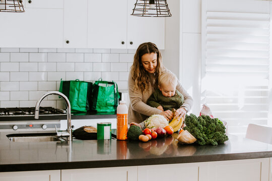 Mum getting a banana for toddler son from unpacked groceries on countertop