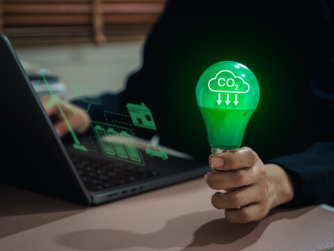 Hand hold green light bulb with CO2 emission icon and digital interface, symbolizing carbon footprint reduction, green energy, climate change awareness, and sustainable technology for cleaner future.