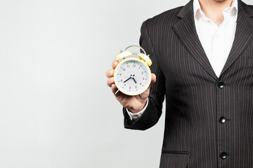 a businessman in suit holding an analog vintage alarm clock with his right hand an a black background