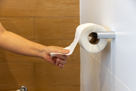 Personal Hygiene Concept: Close-up of Female Hand Tearing off a Sheet of Tissue from a Toilet Roll.