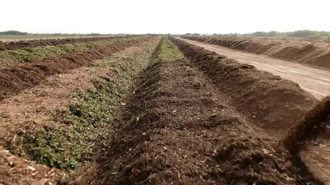 An aerial view shows rows of soil being moved on a farm, with machinery in operation