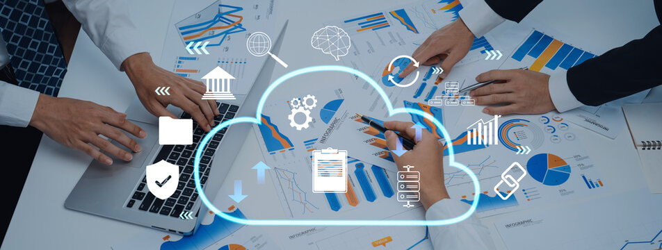 A dynamic business meeting showcasing teamwork with hands analyzing data charts on a table. A laptop and cloud computing icons enhance the collaborative atmosphere. Trope