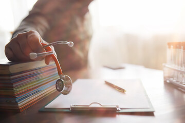 Male doctor search information in book and writtnig prescription, medical stethoscope on the desk at clinic. Medical knowledge and education concept.