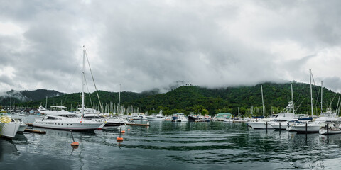 Fototapeta premium Marina of yachts beneath misty hills and cloudy serene skies