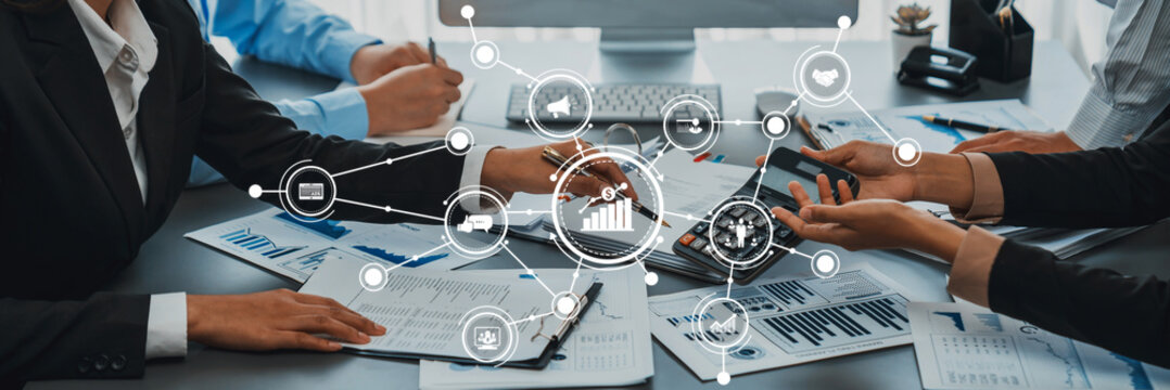 This stock photo features a business meeting scene with professionals analyzing data and discussing strategies, surrounded by digital connectivity illustrations emphasizing collaboration. Amity - Powered by Adobe