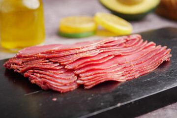 Sliced meat on a dark board with fresh ingredients