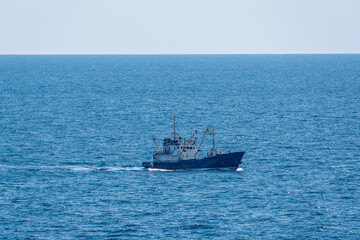 Fishing boat in blue sea and clear sky with birds flying overhead.