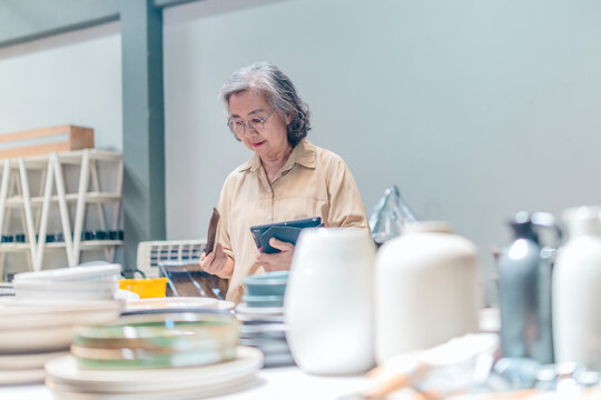 Senior Female Business Owner Inspecting Ceramics - Powered by Adobe