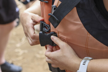 Close up of woman hand fastening black plastic buckle on an orange safety vest strap. She prepares for an outdoor adventure activity, showing concentration