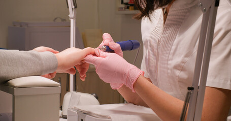 Nail manicure. Salon procedure. Professional woman master hands in protective mask latex sterilized gloves making hardware treatment to female client.