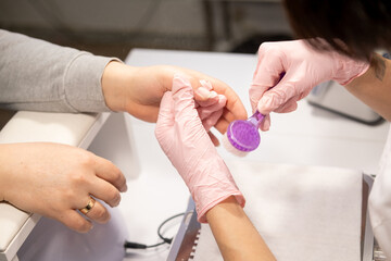 Cleaning hands procedure. Professional manicure therapy. Beauty woman technician in pink medical gloves using brush preparing clients nail fingers for care process.