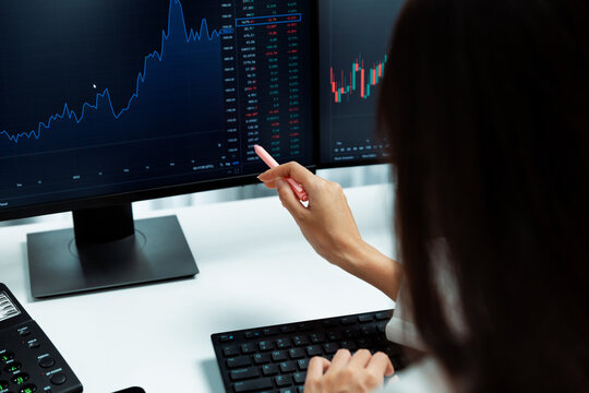 Young beautiful Asian businesswoman pointing with pen in exchange stock market on pc screen at back side view, analyzing profit at modern office, investing high profit valed in wealth. Stratagem.