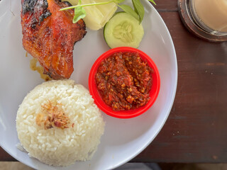 Grilled Chicken with Rice, Sambal, and Fresh Vegetables on a Wooden Table