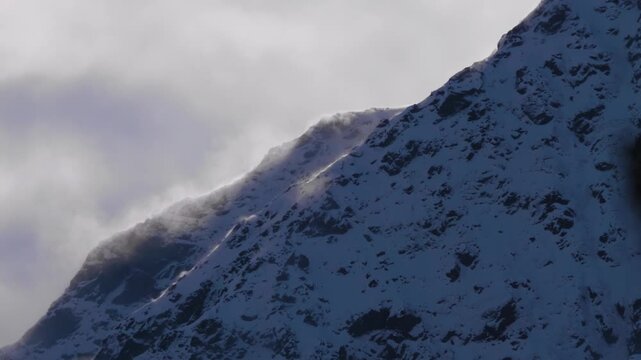 A majestic view of a snow capped mountain peak in the North Caucasus region of Russia. The high altitude landscape is characterized by rugged, rocky terrain covered in a fresh layer of snow, with clou