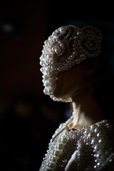 Close-up portrait of a model wearing an avant-garde pearl mask and dress, dramatic low light fashion concept