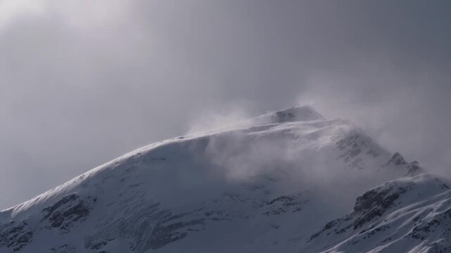 A dramatic close up shot of a snow covered mountain peak in the North Caucasus, Russia. The footage captures the raw power of nature as a strong wind whips up a blizzard, sending clouds of snow swirli