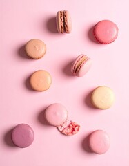 Macarons scattered on pink surface, one slightly broken