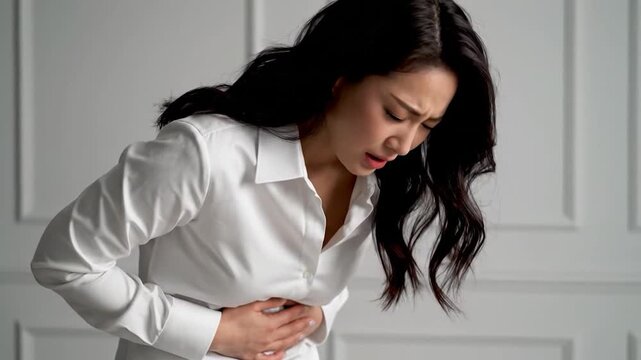 Woman clutches stomach in pain, wearing white shirt