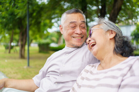 Happy senior Asian couple relaxing together on bench. Retirement couple lifestyles.