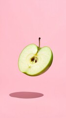 Green apple half floating against a pastel pink background