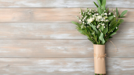 Naklejka premium Rustic DIY flower bouquet wrapped in kraft paper with string, featuring white flowers and green leaves, lies on wooden surface