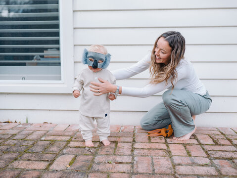 Mother holding and guiding toddler son wearing koala mask