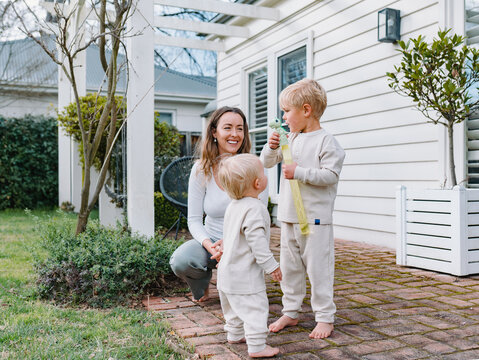Mother crouching on brick patio playing bubbles with two sons