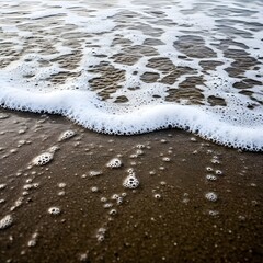 Close-up of gentle ocean waves washing onto a sandy beach with foam and bubbles creating a peaceful seaside scene
