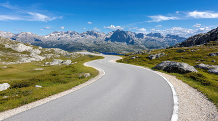Fototapeta premium Winding mountain road with sharp turns offers panoramic view of rugged peaks under clear blue sky, surrounded by rocky terrain and green grass