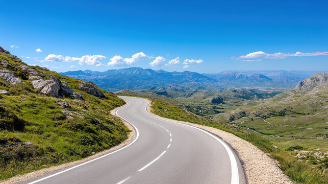 Winding mountain road with sharp turns offers panoramic view of distant peaks under clear blue sky, surrounded by lush green hills and rocky terrain