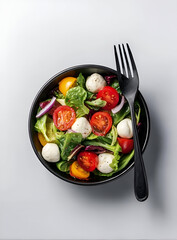 Fresh salad with vibrant tomatoes, mozzarella balls, and leafy greens in a stylish black bowl.