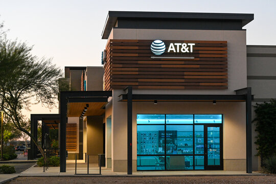 AT&T retail store with illuminated signage and glass display windows, showcasing a telecommunications storefront in a modern commercial retail center at dawn