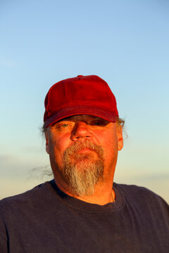 Man with a goatee beard in maroon cap, looking at camera..