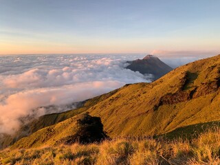 Majestic mountain landscape above the clouds at sunrise. Golden sunlight illuminates grassy slopes and volcanic peaks, creating a serene and breathtaking natural scenery — perfect for themes of advent