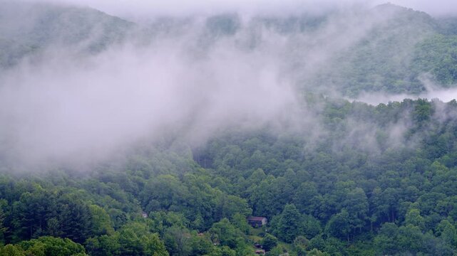 Aerial view gliding over a quiet, fog-covered valley at sunrise.