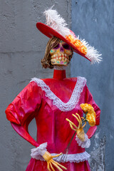 Obraz premium A woman in a red dress with a flower in her hand. The woman is dressed in a skeleton costume. Mexican Day of the Dead tradition, offerings, food, colors, decorations, and papel picado, La Catrina.