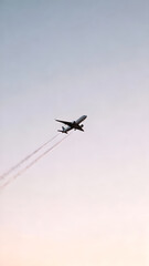 An airplane flying high in the sky, leaving vapor trails against a soft sunset backdrop.