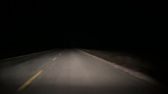 POV of late night travel on an empty country road with headlights cutting through pitch black surroundings. Spooky point of view. 