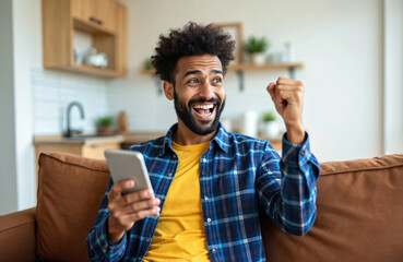 Happy man using smartphone shows excitement. He wins lottery feels joy sitting on couch at home. Person celebrates victory success. Male with mobile phone read good news.