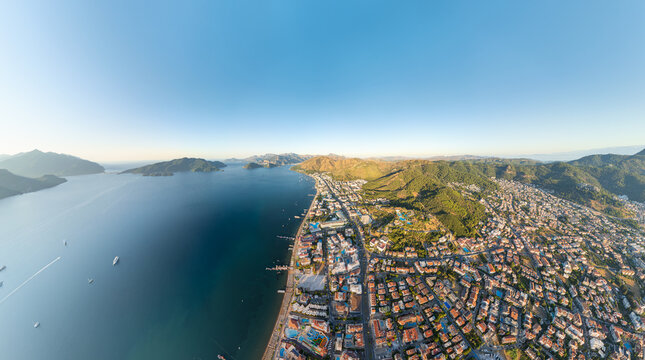 Marmaris, Turkey. Panoramic aerial view of coastline with beaches and hotels, city and forested mountains in morning sunlight. Coastal urban landscape. Aerial view. - Powered by Adobe