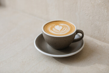 A cappuccino with a heart-shaped pattern on the foam in a stunning ceramic cup against a neutral background.