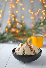 Bowl of homemade Christmas tree-shaped cookies with sugar, a yellow mug, and festive bokeh lights in the background creating a warm, cozy holiday atmosphere.