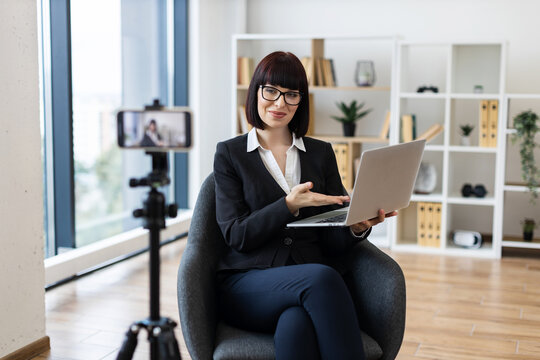 Caucasian woman, young adult, recording video blog with laptop indoors, discussing business.