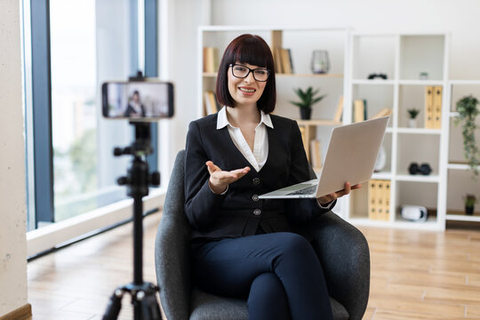 Caucasian woman, young adult, recording video blog with laptop indoors, discussing business.